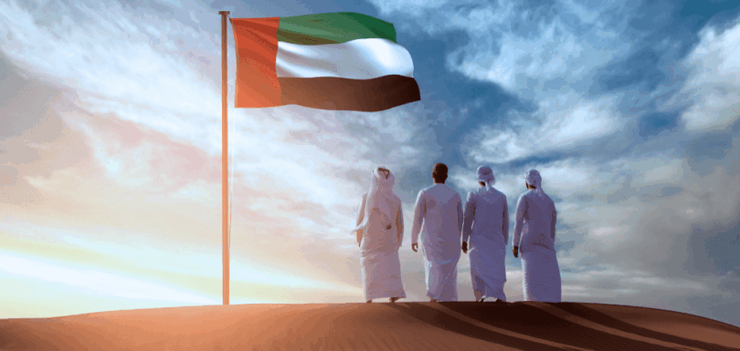 Emiratis standing in the desert by the UAE flag on National Day