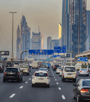 Heavily congested urban highway in Dubai, with numerous vehicles of different sizes and types stuck in traffic, surrounded by a backdrop of tall skyscrapers and modern high-rise buildings